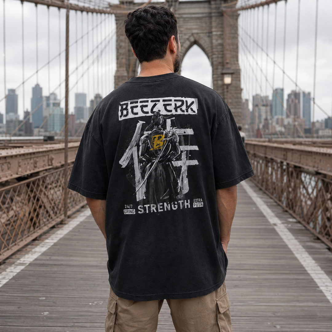 Man wearing a faded black oversized Beezerk samurai strength back-print T-shirt on the Brooklyn Bridge.