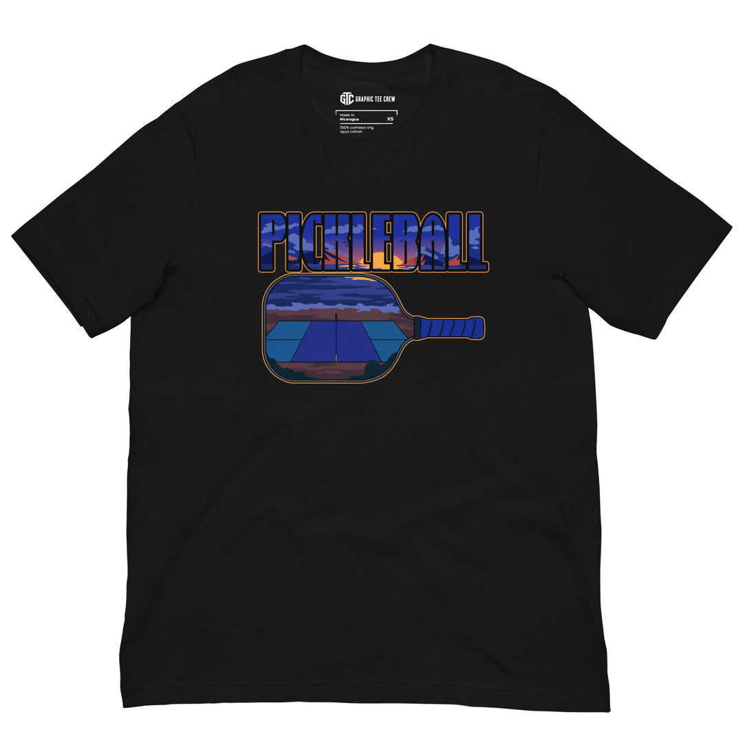 Sunset Court Pickleball T-Shirt featuring a mountain sunset and outdoor court inside bold pickleball lettering and a paddle graphic.