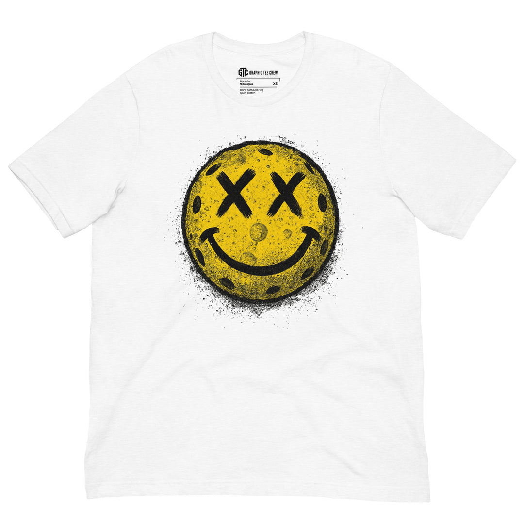 Distressed pickleball smiley face graphic T-shirt featuring a yellow ball with X-shaped eyes and a gritty black splatter effect